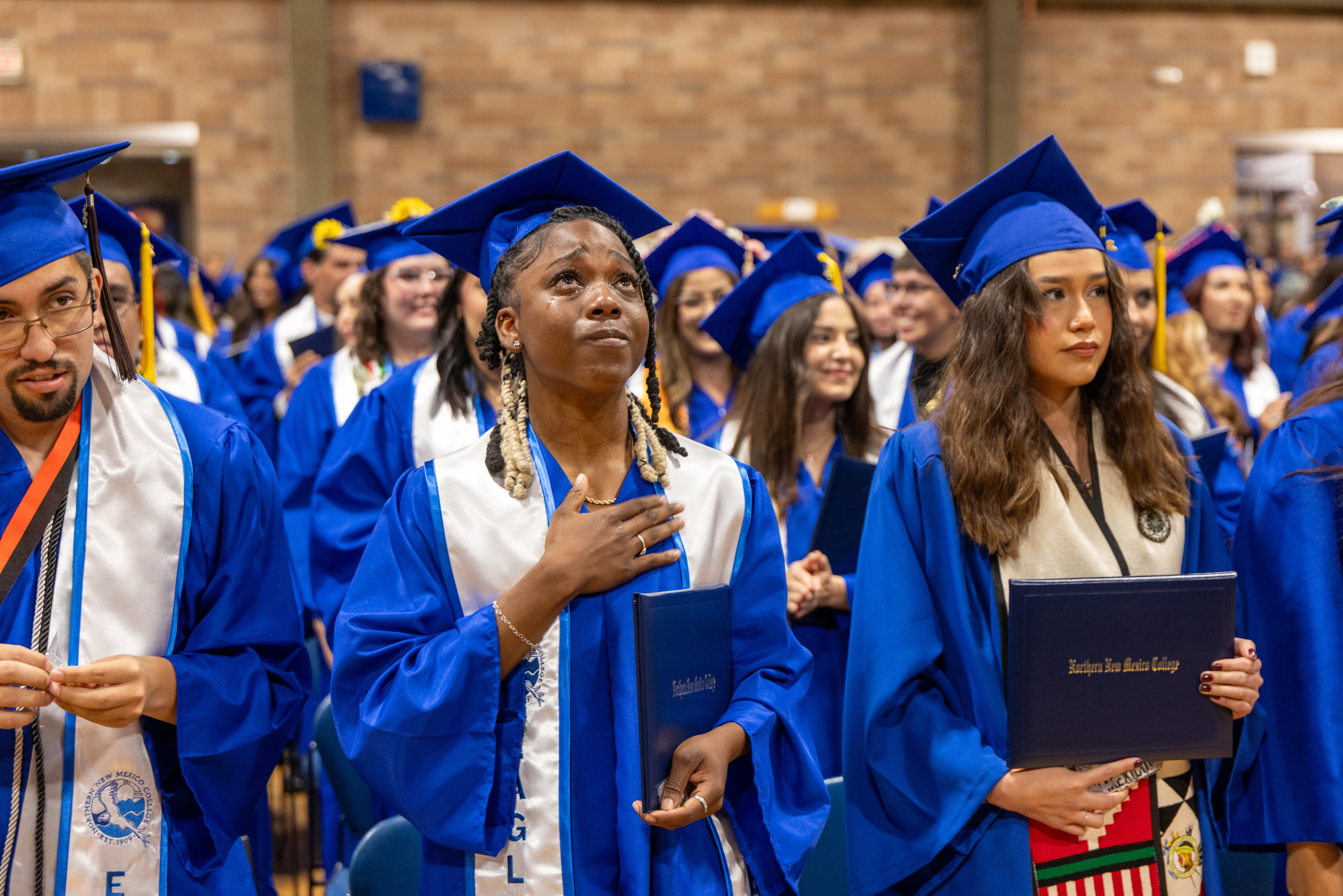 An image of an NNMC graduating class, focused on a black graduate with her left hand over her heart, looking skyward with intense emotion.
